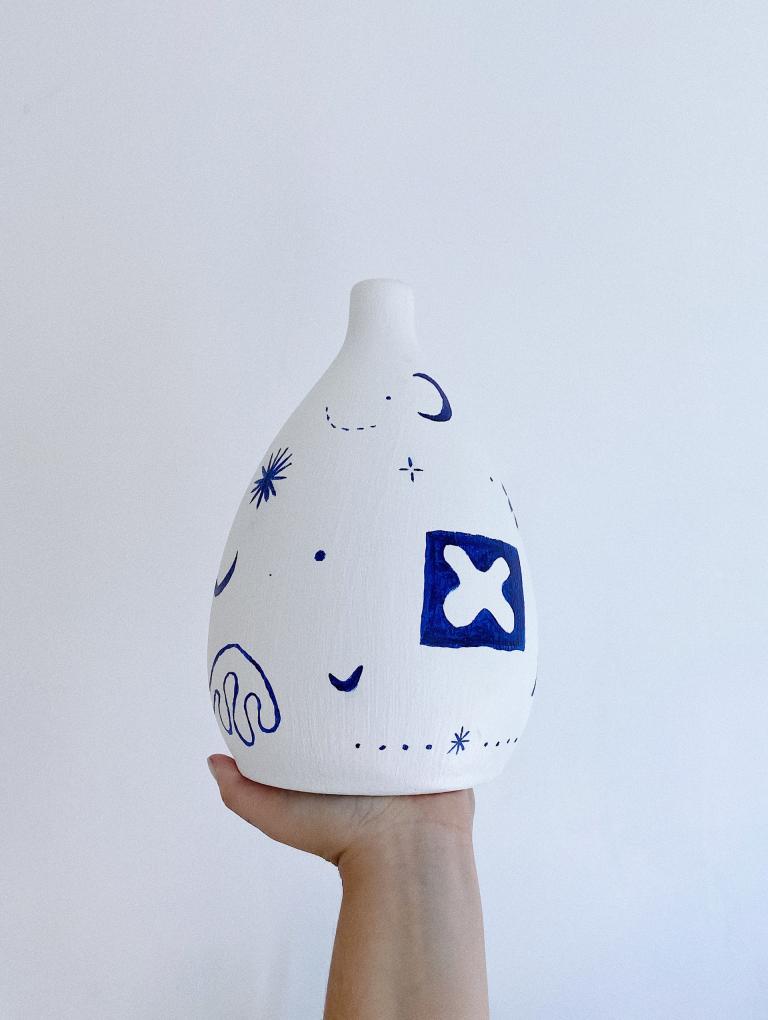 Hand holding a white vase that is painted with blue markings.