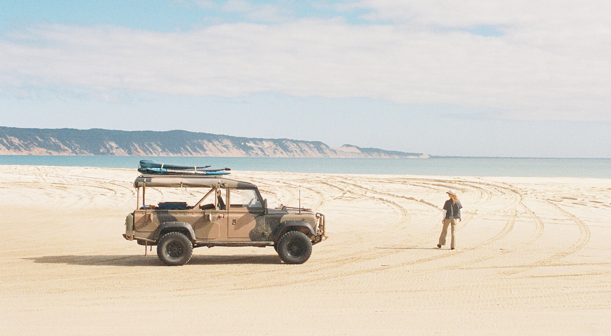 A person stood next to an old car on a beach.